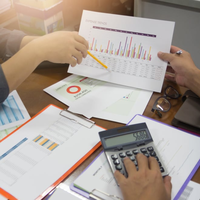Hände mit Finanzdiagrammen und Unterlagen auf einem Tisch